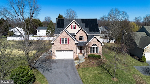 traditional-style house with an attached garage, solar panels, brick siding, a shingled roof, and driveway