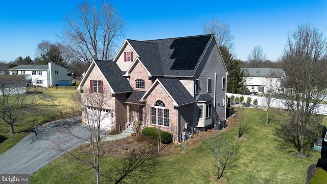 view of front of home featuring an attached garage, solar panels, brick siding, concrete driveway, and a front yard