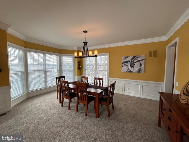 carpeted dining area with an inviting chandelier, ornamental molding, and a healthy amount of sunlight