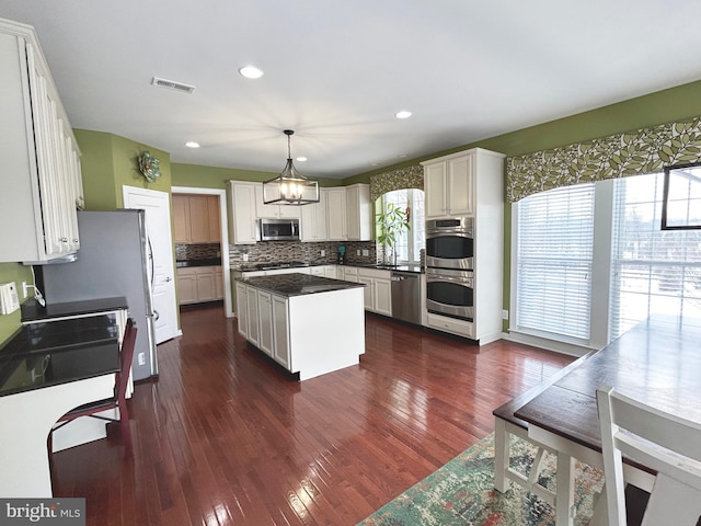 kitchen with stainless steel appliances, a kitchen island, white cabinets, and pendant lighting