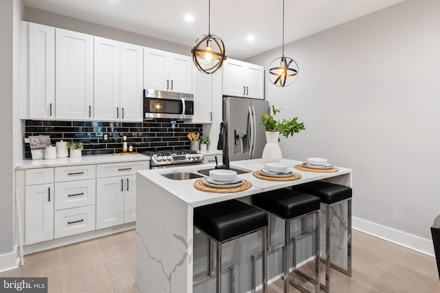 kitchen with an island with sink, stainless steel appliances, decorative light fixtures, white cabinets, and a breakfast bar