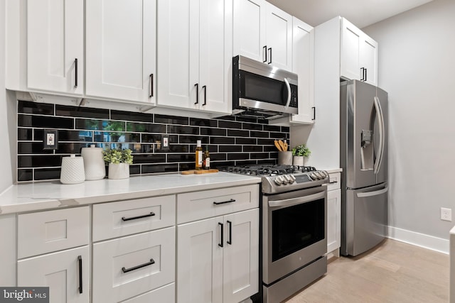 kitchen with appliances with stainless steel finishes, white cabinetry, light hardwood / wood-style floors, decorative backsplash, and light stone counters