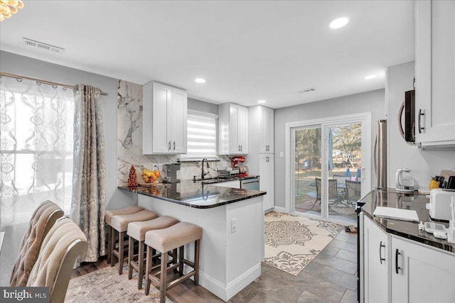 kitchen with dark stone counters, a breakfast bar, white cabinetry, and sink