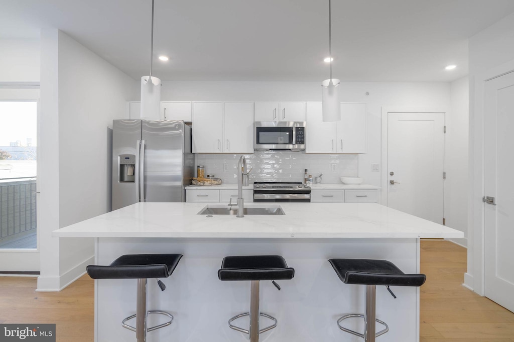 kitchen featuring stainless steel appliances, white cabinets, pendant lighting, and an island with sink