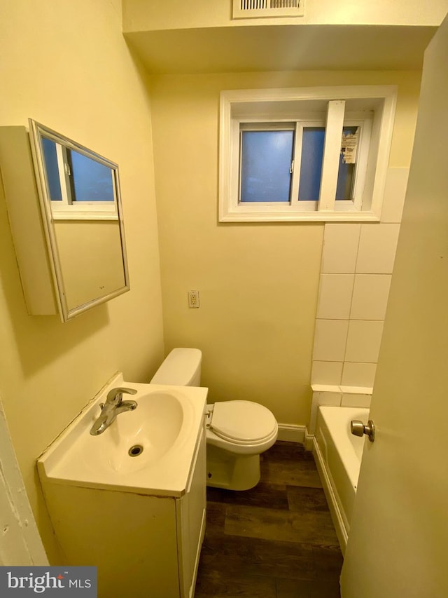 bathroom featuring wood-type flooring, a bathtub, vanity, and toilet