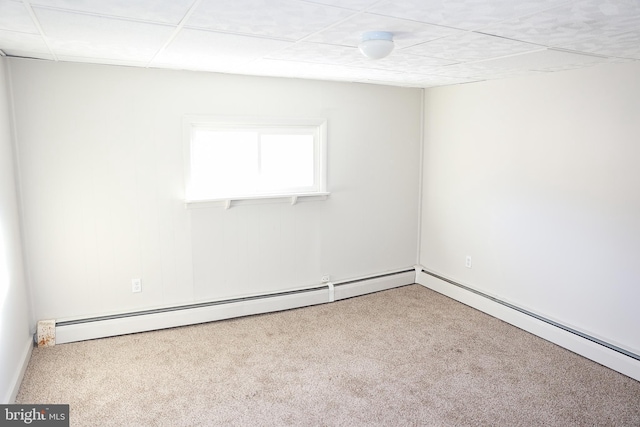 carpeted empty room featuring a baseboard heating unit and a drop ceiling