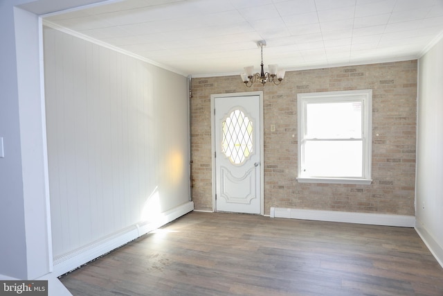 foyer with brick wall, dark wood-type flooring, crown molding, and a chandelier