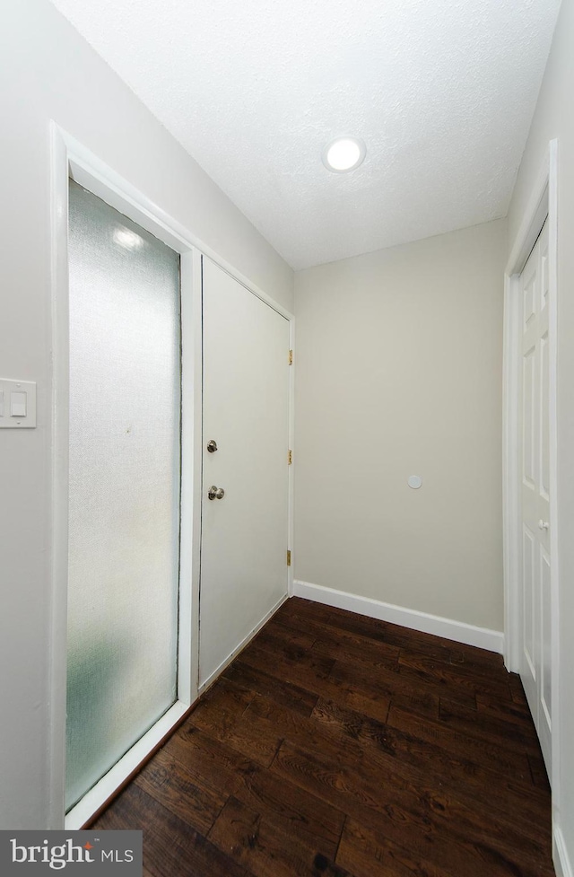 hallway with a textured ceiling and dark hardwood / wood-style floors