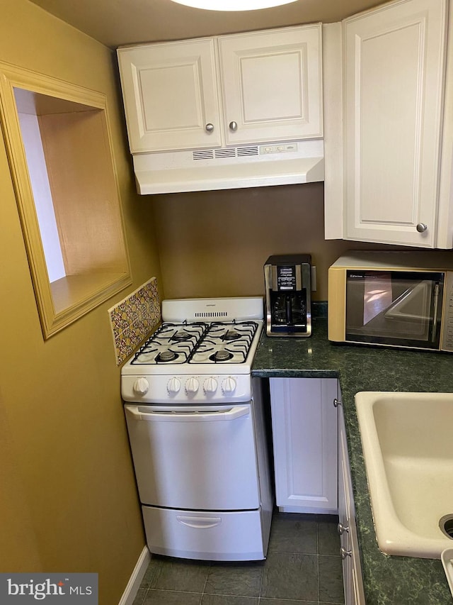 kitchen featuring sink, dark tile patterned flooring, white cabinetry, and gas range gas stove