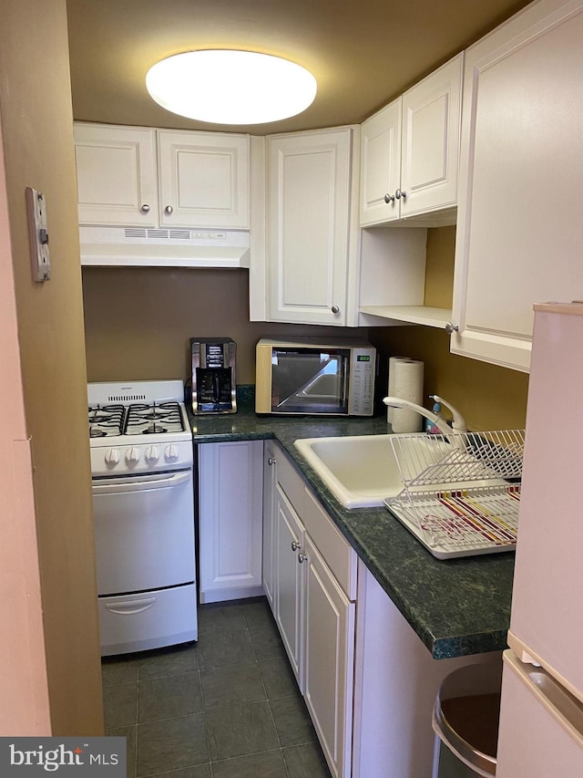 kitchen with white appliances, sink, dark tile patterned floors, and white cabinetry