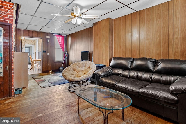 living room with wooden walls, a drop ceiling, ceiling fan, and light wood-type flooring