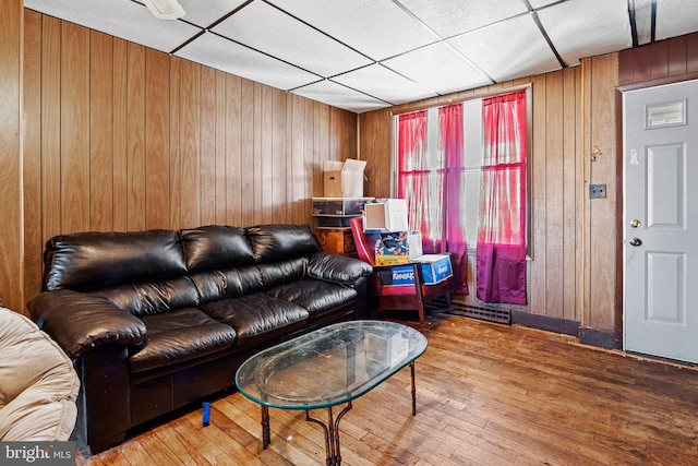 living room featuring wood-type flooring, wood walls, and a drop ceiling