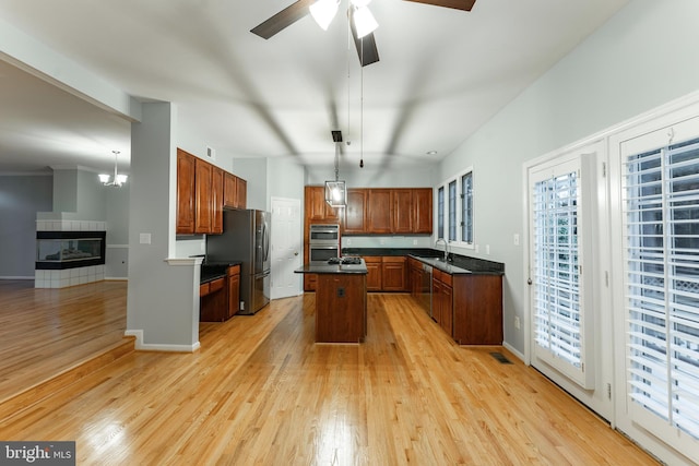 kitchen with sink, hanging light fixtures, a kitchen island, stainless steel appliances, and light hardwood / wood-style floors