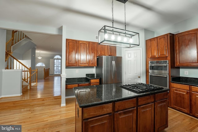 kitchen featuring appliances with stainless steel finishes, light hardwood / wood-style floors, a kitchen island, decorative light fixtures, and dark stone counters