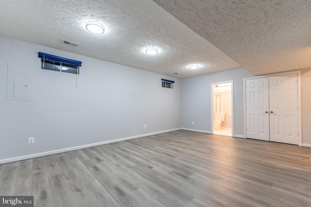 basement featuring electric panel, a textured ceiling, and light wood-type flooring