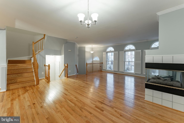 unfurnished living room with crown molding, a notable chandelier, a fireplace, and light wood-type flooring