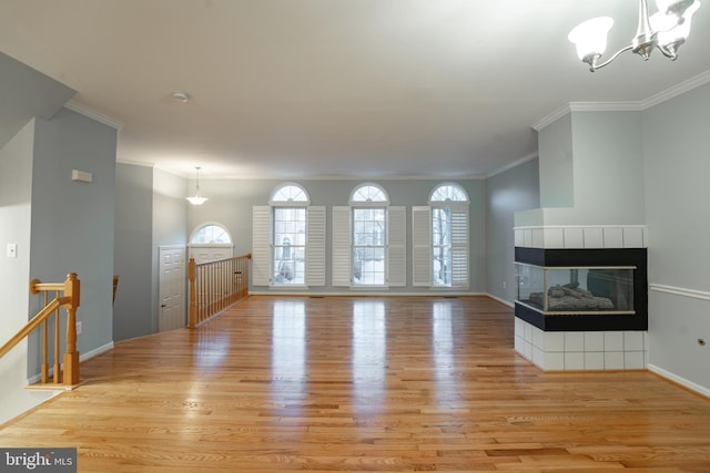 unfurnished living room with a tiled fireplace, ornamental molding, light hardwood / wood-style floors, and an inviting chandelier