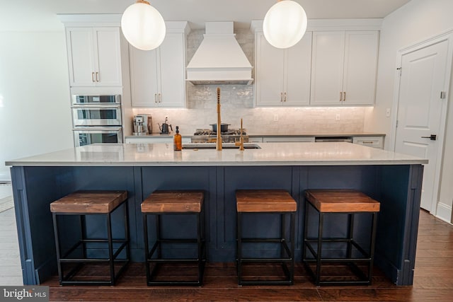 kitchen featuring stainless steel double oven, white cabinetry, backsplash, light stone countertops, and custom range hood