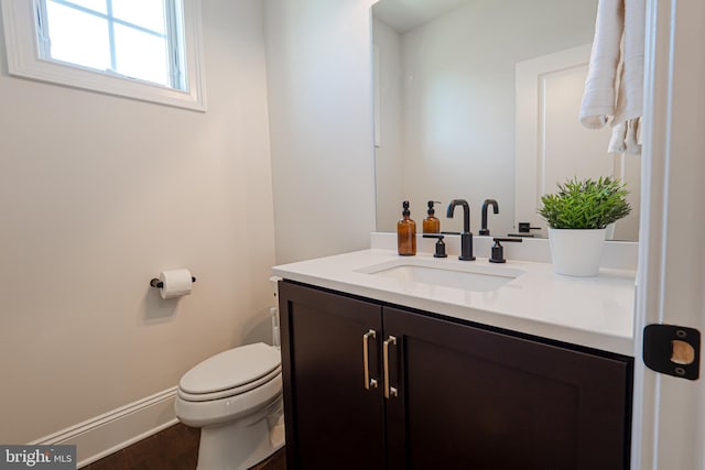 half bath featuring baseboards, vanity, toilet, and wood finished floors