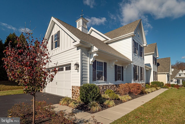 view of side of property with driveway, stone siding, an attached garage, a yard, and board and batten siding