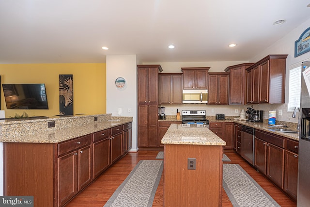 kitchen with stainless steel appliances, light stone countertops, kitchen peninsula, a kitchen island, and sink