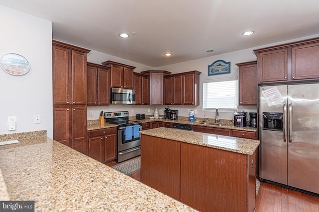 kitchen with stainless steel appliances, sink, hardwood / wood-style floors, kitchen peninsula, and light stone countertops