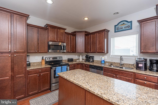 kitchen with wood-type flooring, appliances with stainless steel finishes, light stone counters, sink, and tasteful backsplash