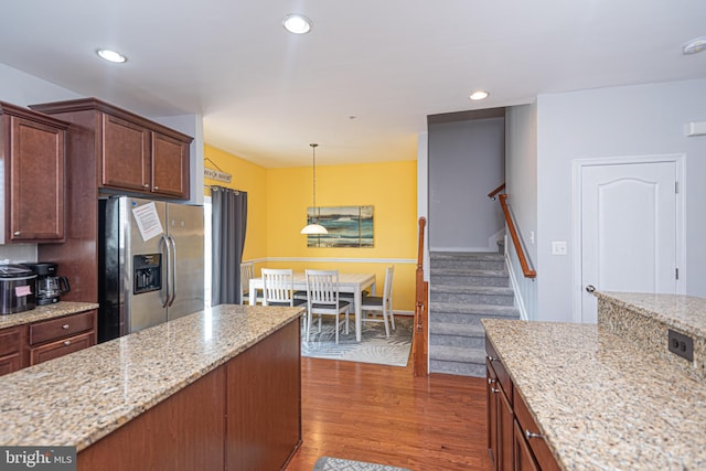 kitchen featuring light stone counters, wood-type flooring, stainless steel refrigerator with ice dispenser, and hanging light fixtures