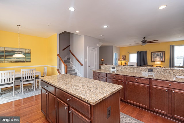 kitchen with light stone countertops, ceiling fan, dark wood-type flooring, a kitchen island, and decorative light fixtures