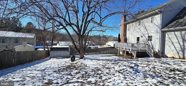 snowy yard featuring a wooden deck and a storage unit