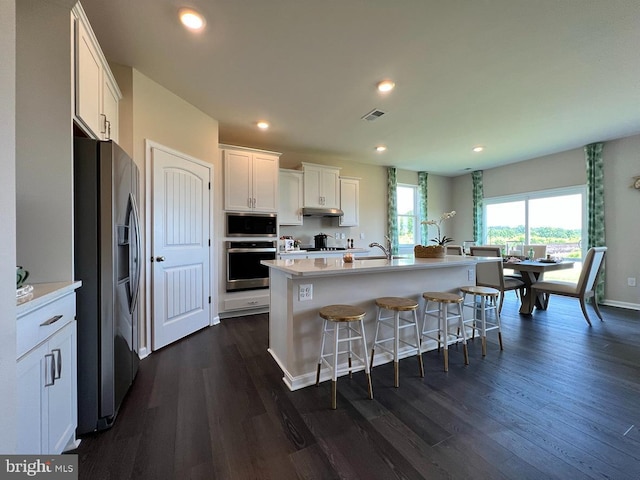 kitchen featuring dark wood-type flooring, an island with sink, a kitchen bar, white cabinets, and appliances with stainless steel finishes