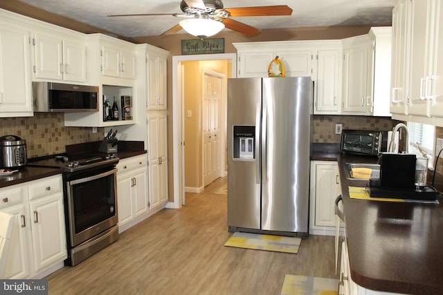 kitchen featuring white cabinets, ceiling fan, light wood-type flooring, tasteful backsplash, and appliances with stainless steel finishes