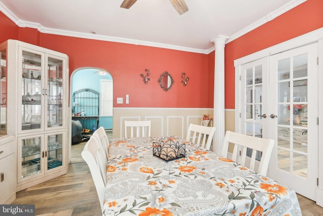 dining area featuring arched walkways, french doors, a wainscoted wall, ornamental molding, and wood finished floors