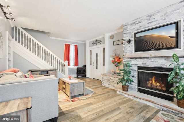 living room with wood finished floors, crown molding, a stone fireplace, and stairs