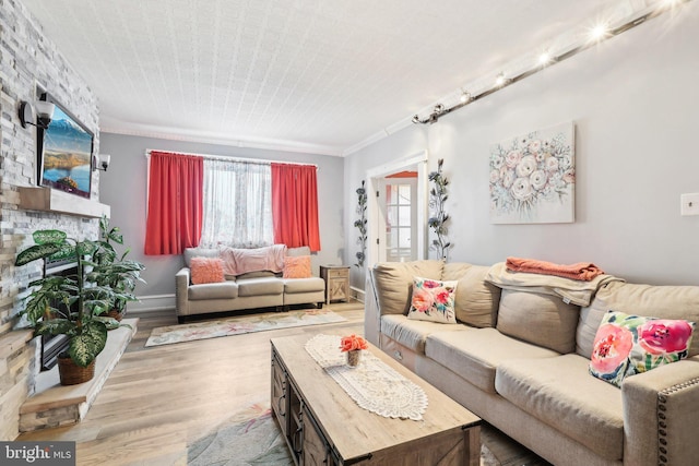 living area with ornamental molding, a fireplace, baseboards, and wood finished floors