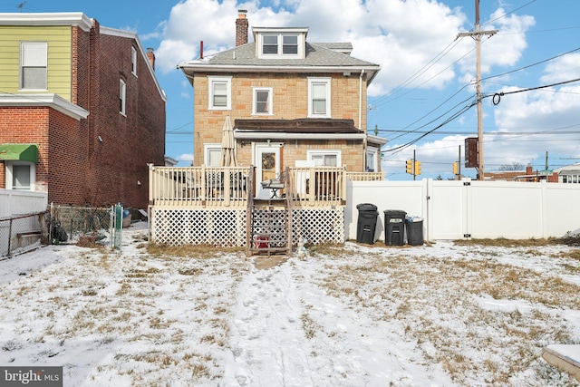 snow covered rear of property with stone siding, a fenced backyard, a gate, and a deck