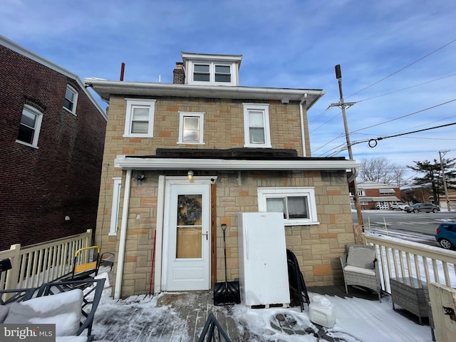 snow covered back of property with stone siding