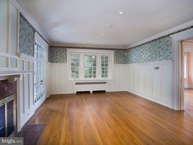 interior space featuring radiator, hardwood / wood-style floors, plenty of natural light, ornamental molding, and a brick fireplace