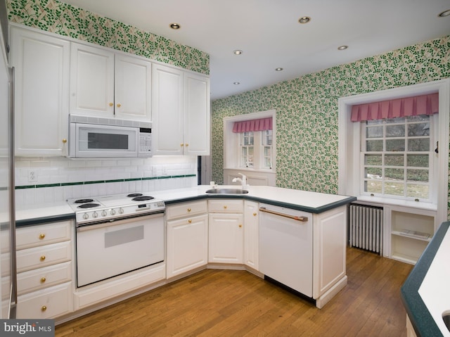 kitchen with radiator, sink, white cabinets, and white appliances