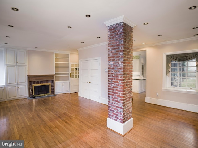 unfurnished living room with decorative columns, crown molding, a fireplace, and light wood-type flooring