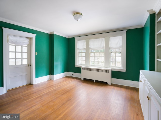 empty room with crown molding, radiator, a wealth of natural light, and light hardwood / wood-style flooring