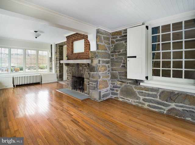 unfurnished living room featuring wood-type flooring, wooden ceiling, ornamental molding, radiator heating unit, and a fireplace