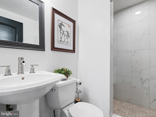 bathroom featuring toilet, a tile shower, and sink