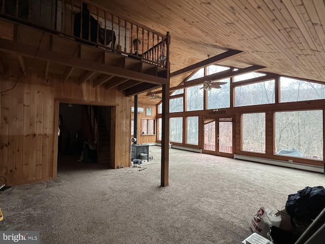 unfurnished living room with ceiling fan, wooden walls, baseboard heating, and plenty of natural light