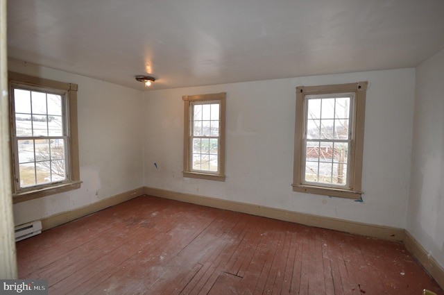 empty room with a baseboard heating unit, a wealth of natural light, and wood-type flooring