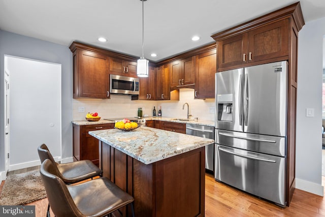 kitchen with stainless steel appliances, light wood-type flooring, pendant lighting, light stone counters, and sink