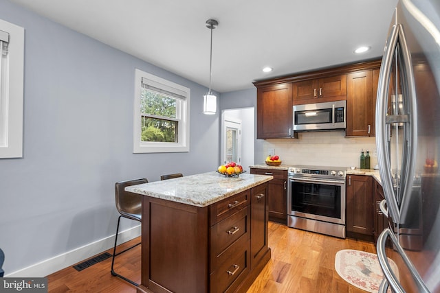 kitchen featuring decorative light fixtures, a breakfast bar, tasteful backsplash, a kitchen island, and appliances with stainless steel finishes