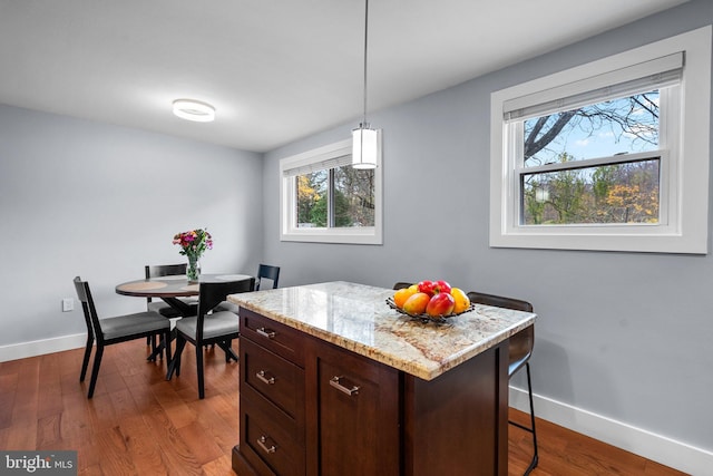 kitchen with a kitchen breakfast bar, a center island, hardwood / wood-style flooring, dark brown cabinets, and decorative light fixtures