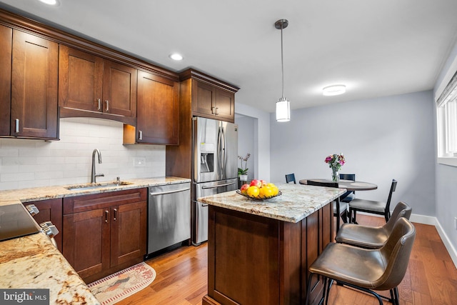 kitchen featuring light stone counters, light hardwood / wood-style flooring, decorative light fixtures, appliances with stainless steel finishes, and sink