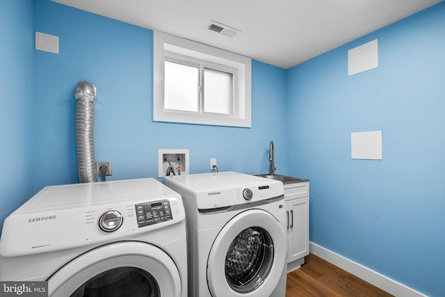 laundry room featuring dark wood-type flooring, cabinets, washing machine and clothes dryer, and sink